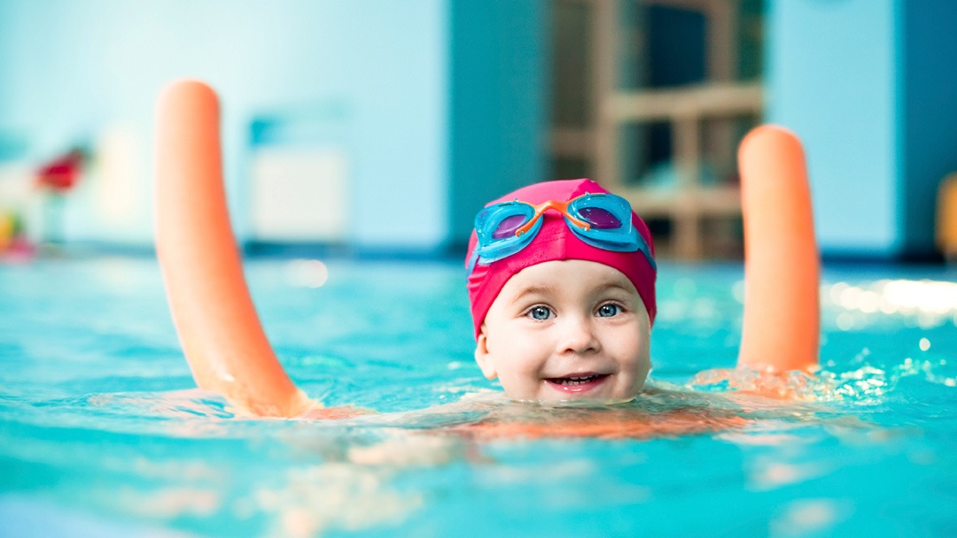 Child in a swimming pool, only head visible, playing with a float
