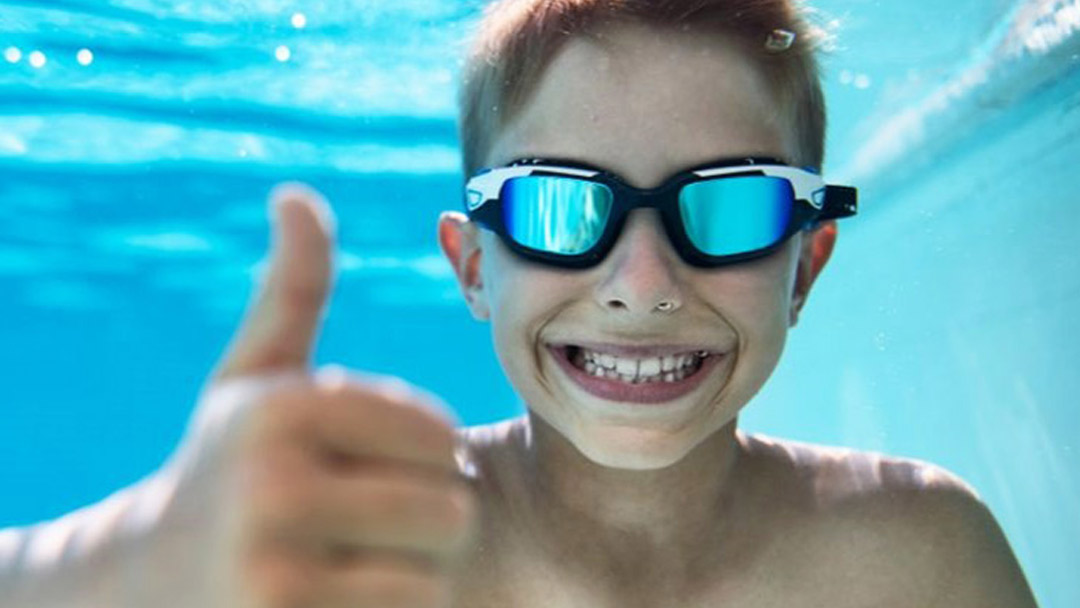 Boy doing a thumbs up under water, smiling and looking happy