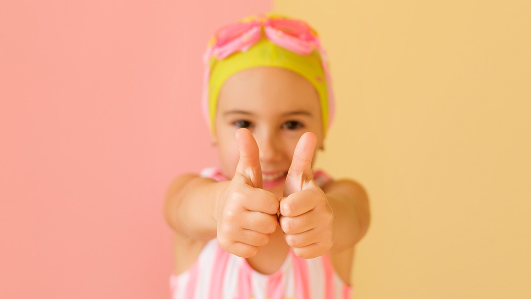Girl in swimming costume holding both thumbs up in front of her.